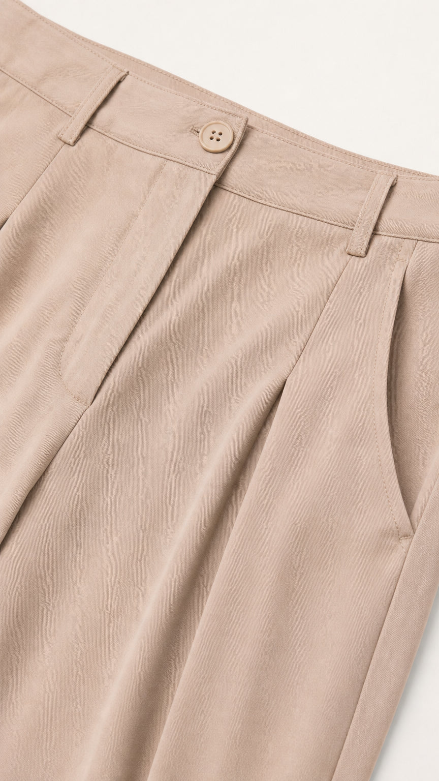 Close-up detail of beige trouser waistband, button closure, belt loops, and front pleating